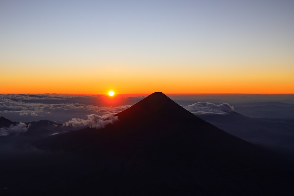 the sun is setting over a mountain with clouds