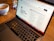 A laptop is open on a wooden table with a webpage displaying '100 ChatGPT audience building prompts' visible on the screen. In the background, there is a bowl of coffee, which seems partially full.