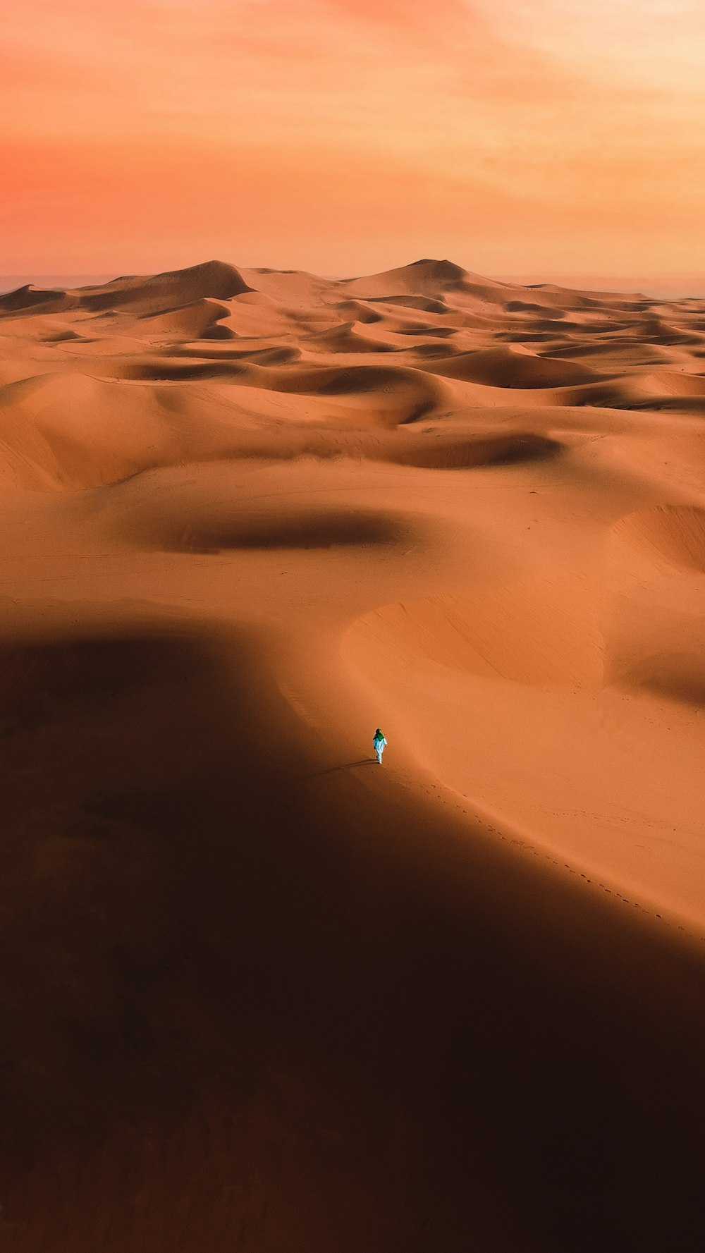 a lone person walking across a desert at sunset