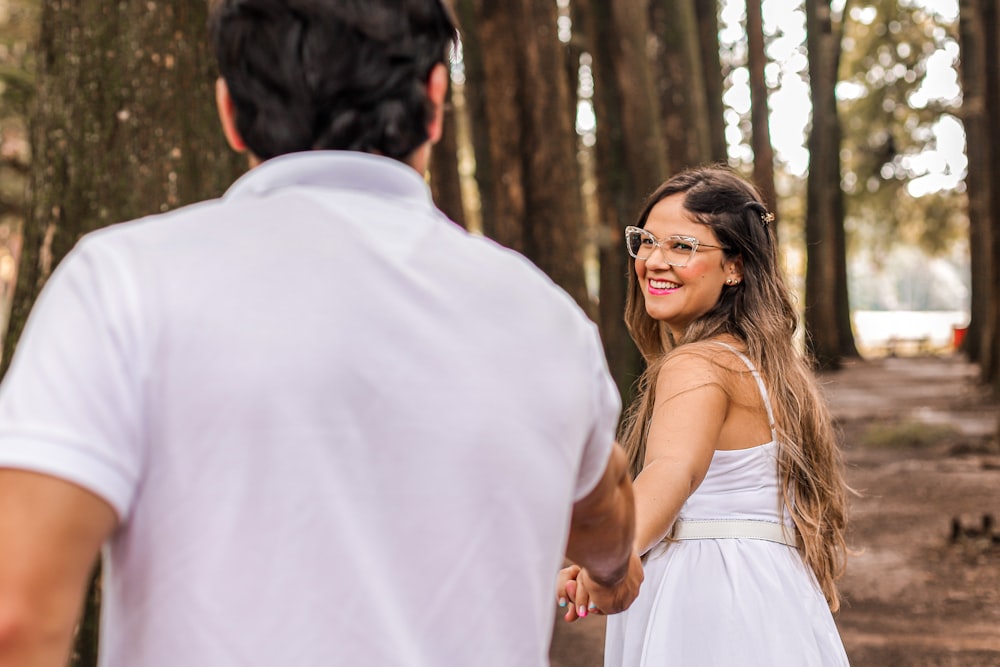 a woman in a white dress holding hands with a man in a white shirt