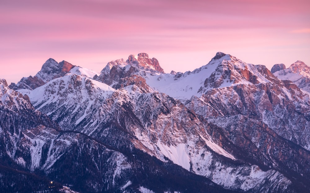 a mountain range covered in snow under a pink sky