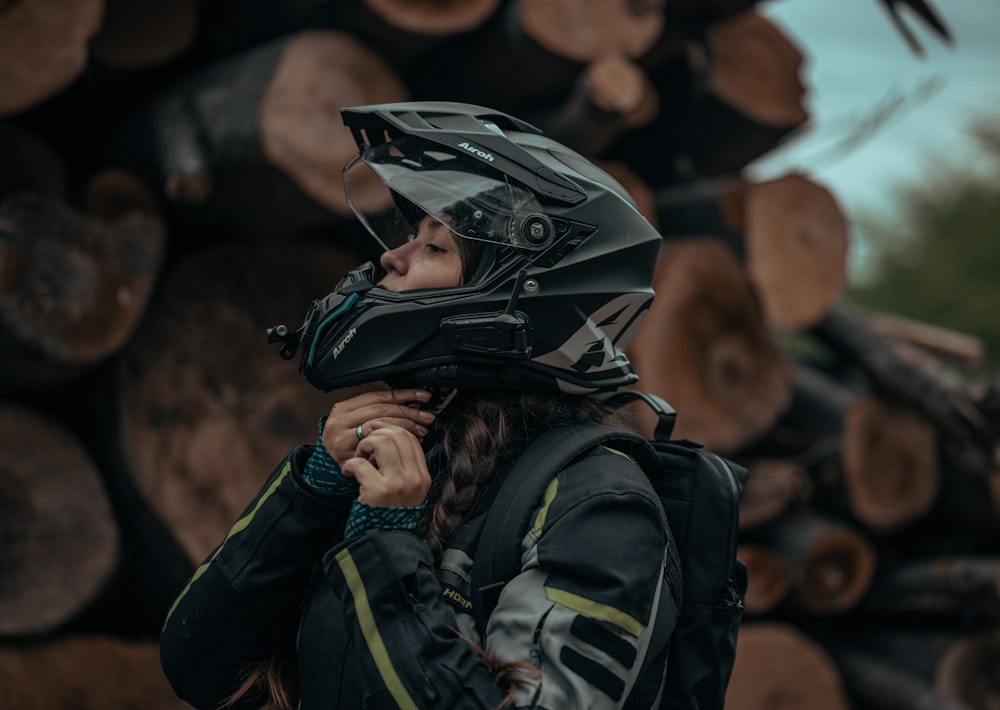 a woman wearing a helmet standing in front of a pile of logs