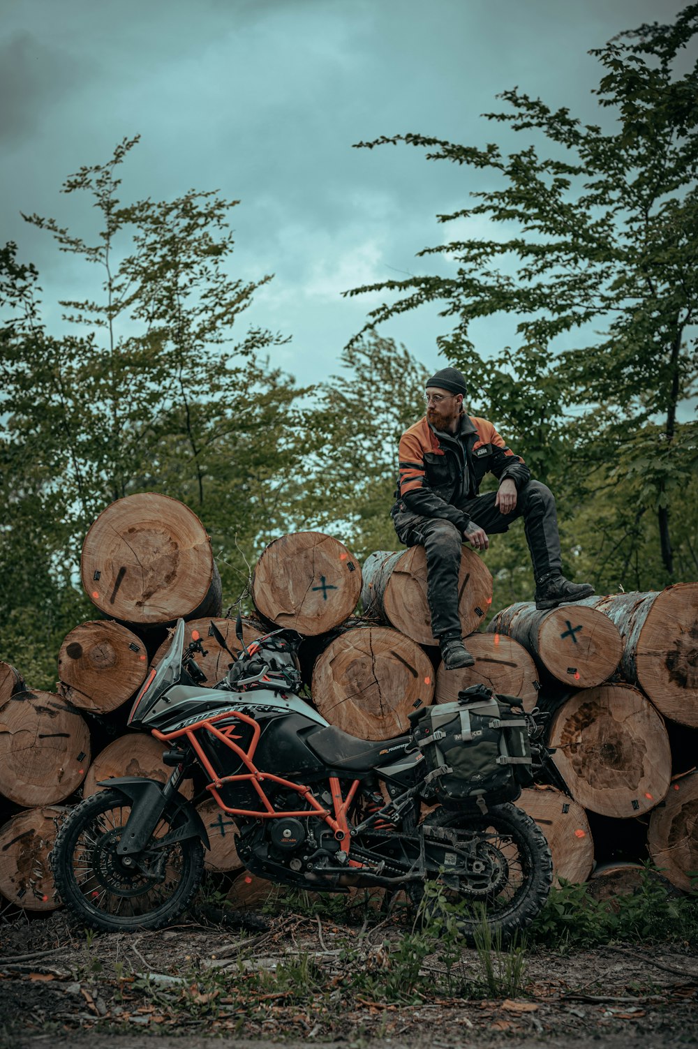 a man sitting on top of a pile of logs next to a motorcycle
