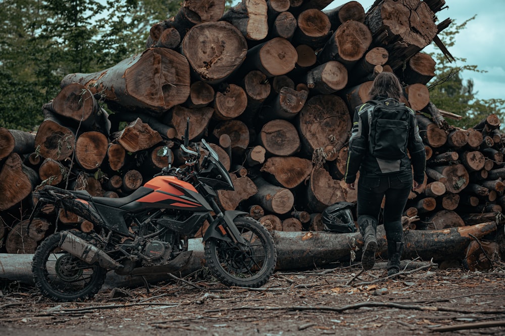 a man standing next to a motorcycle in front of a pile of logs