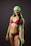 A woman is wearing a vibrant swimsuit consisting of pink, black, and green colors. She has a bright smile and is accessorized with a matching green headscarf. Her posture is confident, and she has visible tattoos on her arms and stomach.