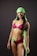 A woman is wearing a vibrant swimsuit consisting of pink, black, and green colors. She has a bright smile and is accessorized with a matching green headscarf. Her posture is confident, and she has visible tattoos on her arms and stomach.