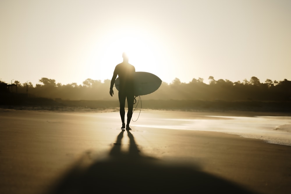 una persona che cammina su una spiaggia con una tavola da surf