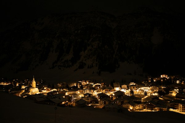A lit-up Alpine village at night below a dark mountain