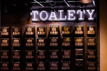 A wall with multiple electrical panels is displayed. Above the panels, a neon sign reads 'TOALETY', which suggests a public restroom indicator. The setup is industrial with a utilitarian aesthetic, featuring dark tones and exposed wiring.