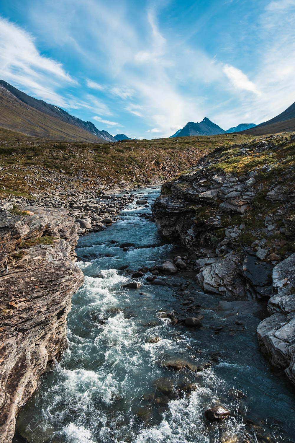 a river running through a rocky valley under a blue sky