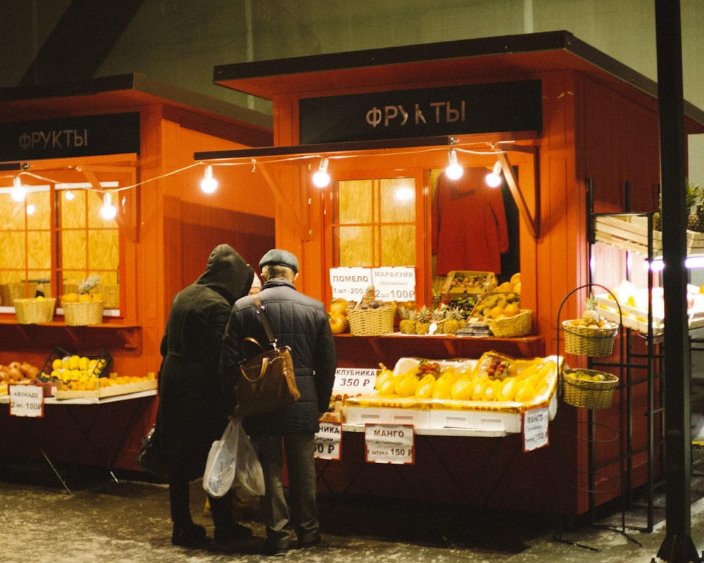a couple of people standing in front of a fruit stand