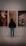 A person is standing in front of three abstract portraits displayed on a wall. The person is viewing the artworks closely, suggesting interest and engagement. The portraits each have distinct features, with the left one showing a face illuminated by a bright light, the center one having a blurred, warm-toned appearance, and the right one depicting a prominent eye.
