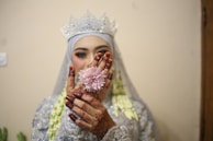 A bride’s delicate hand adorned with intricate henna, holding a bouquet of white orchids against a minimalist backdrop.