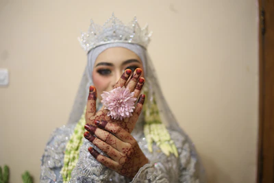 A joyful bride showing her mehndi-stained palms, framed by lush green foliage with subtle henna floral accents.