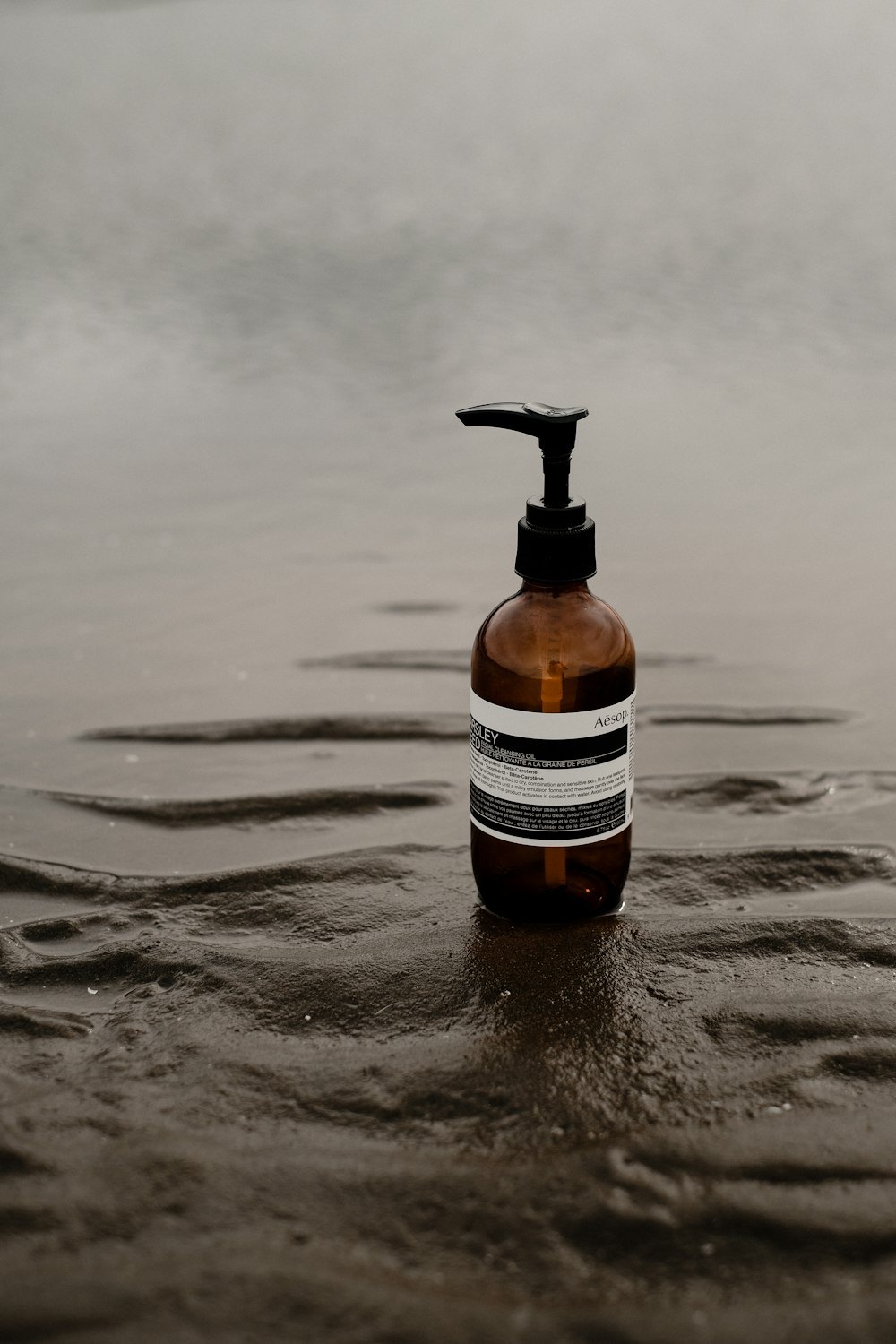 a bottle of soap sitting on top of a wet beach