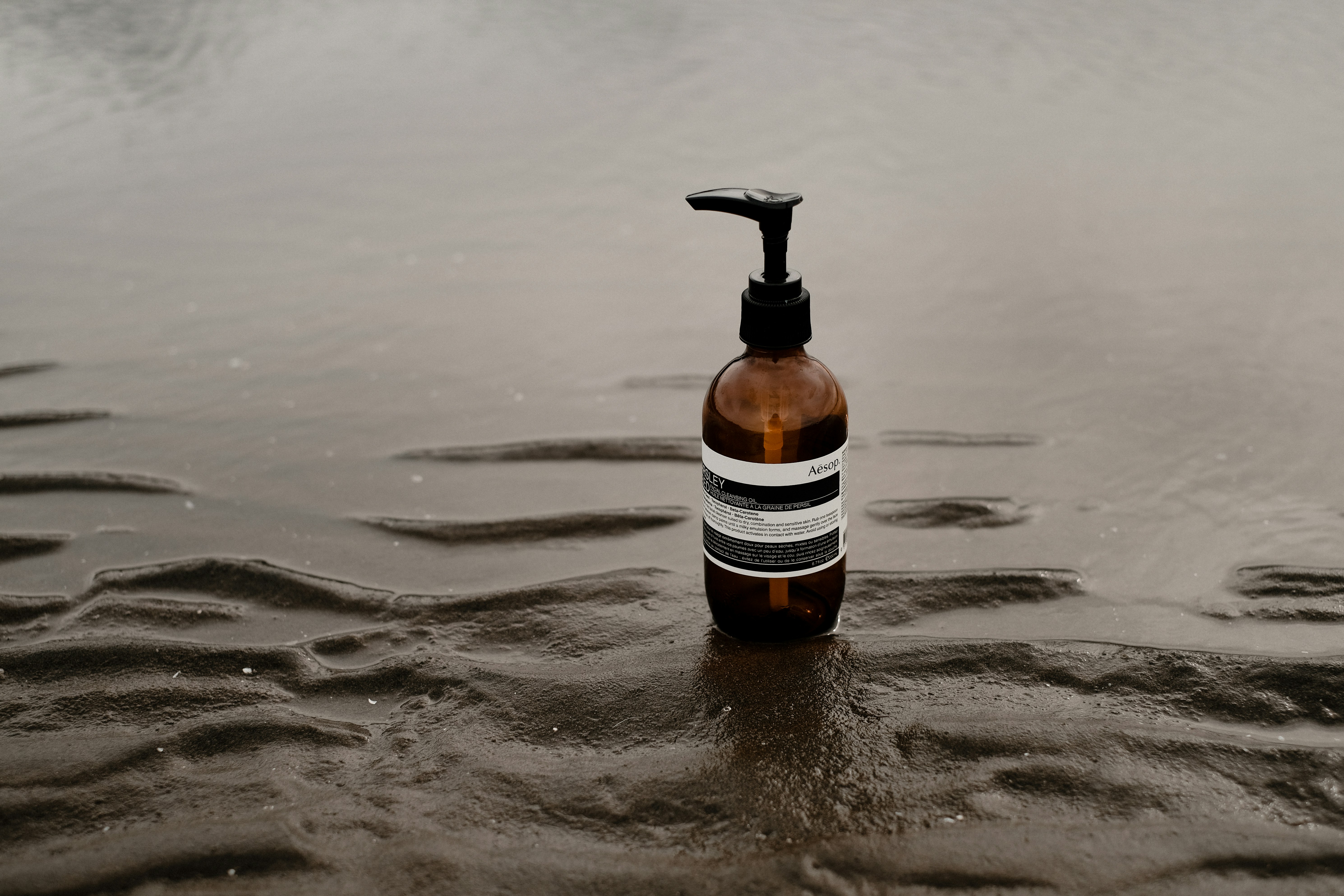 a bottle of soap sitting on top of a wet beach