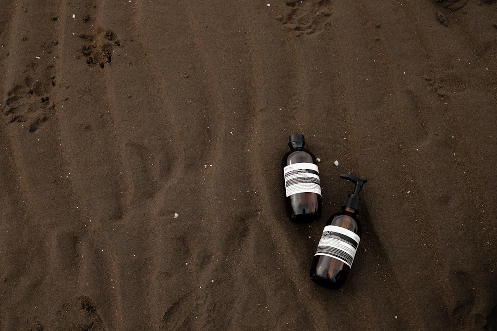 two empty beer bottles laying on a beach