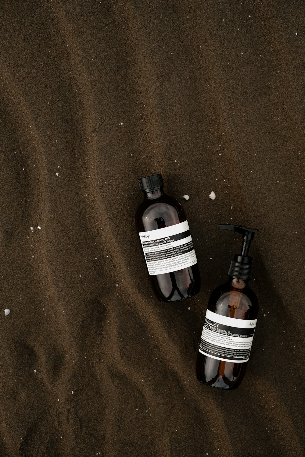 a couple of bottles of soap sitting on top of a sandy beach
