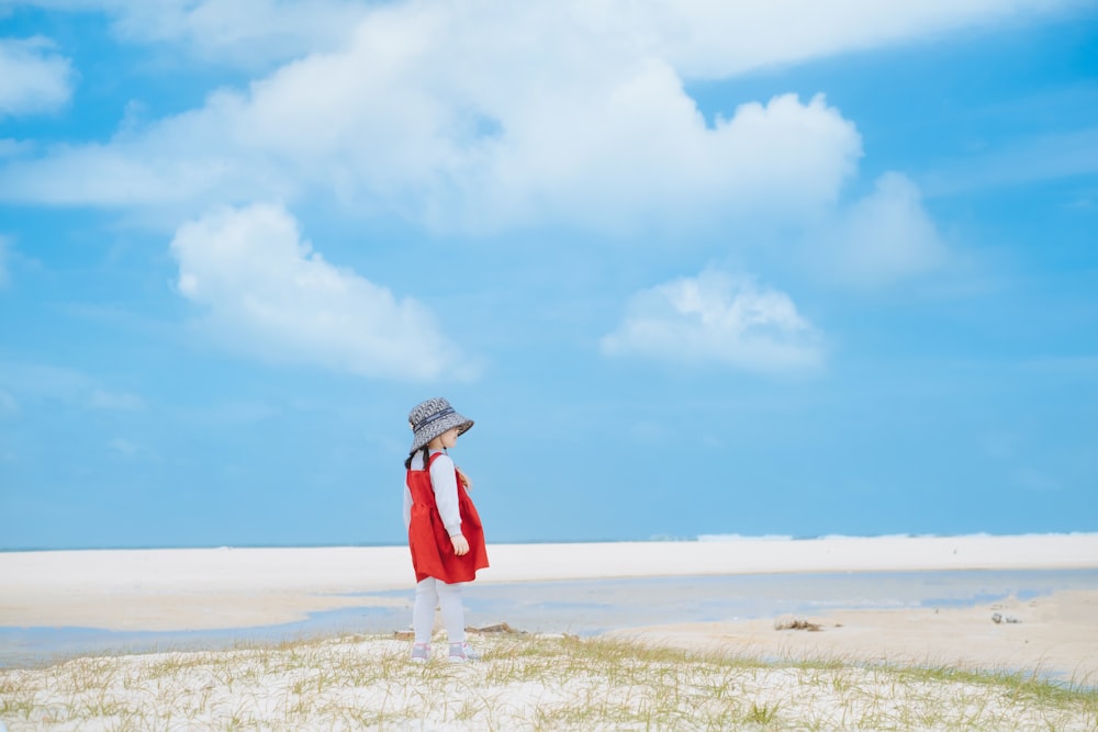 Una mujer con un abrigo rojo y sombrero de pie en una playa