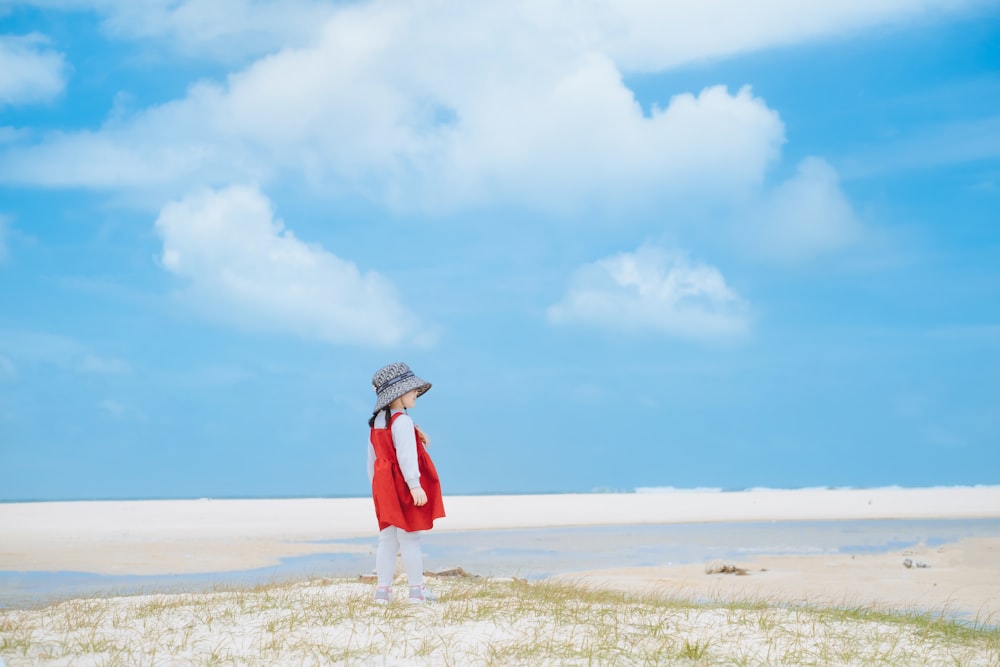 a woman in a red coat and hat standing on a beach