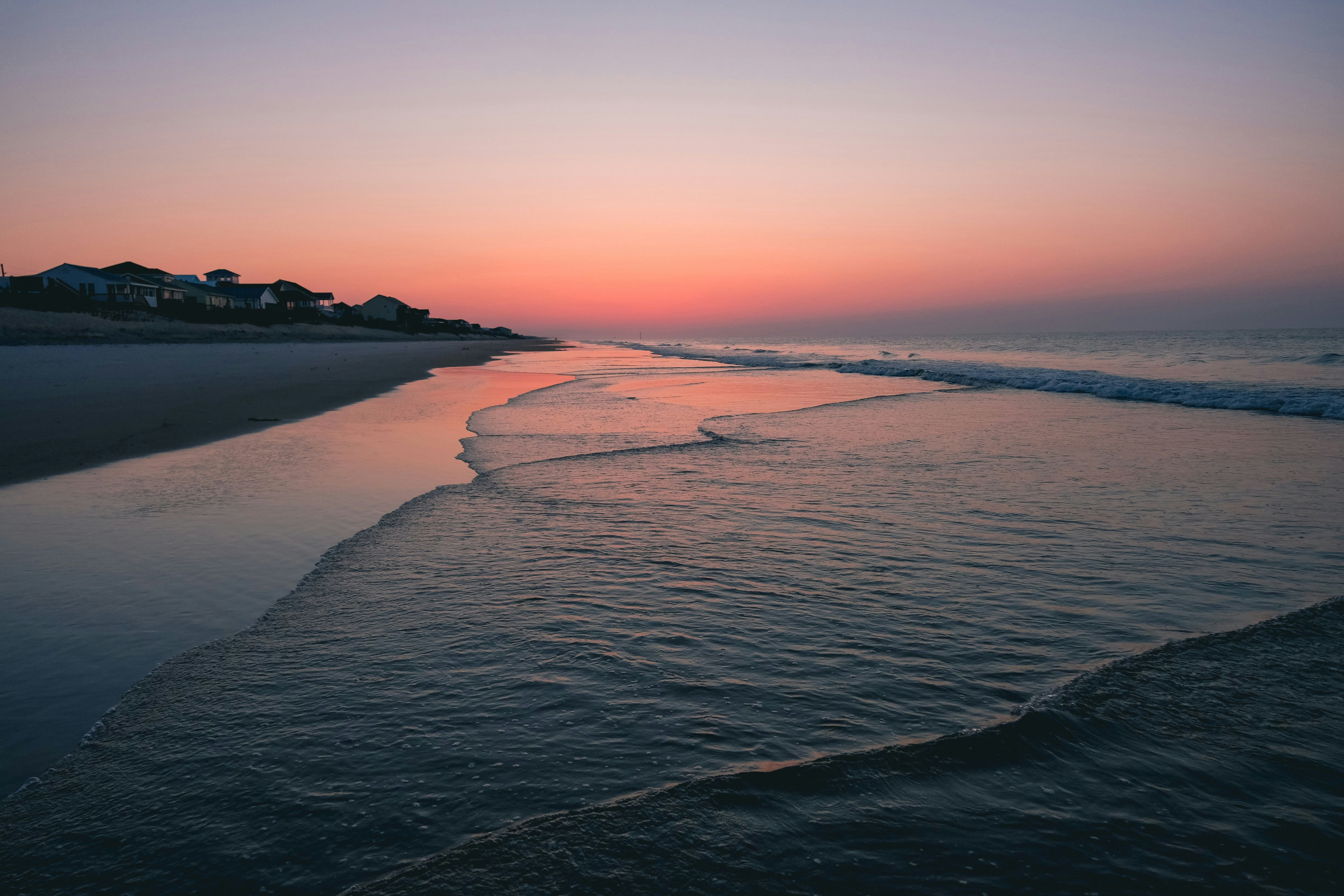 the sun is setting over the water at the beach