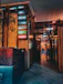 A hallway with wooden walls and various illuminated signs in neon colors pointing to different services such as 'Shiatsu', 'Traditional', and 'Face Therapy'. There is a colorful painting of a Geisha on one wall. The floor is marble, reflecting the lights, and the atmosphere is somewhat dim.