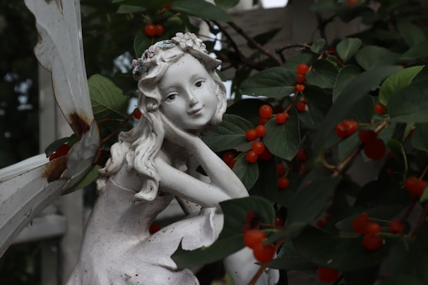 Elegant handcrafted porcelain fairy figurine perched on a mossy log amidst tiny flowers.