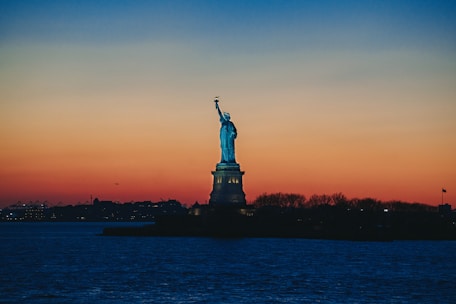 Iconic New York City skyline at sunset with the Statue of Liberty in view.