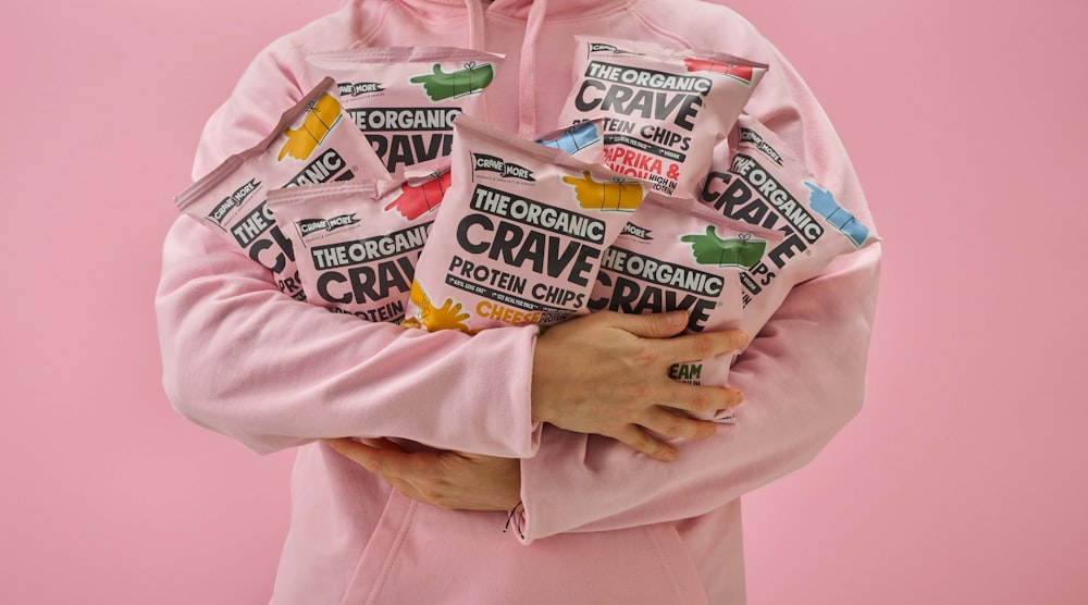 a woman in a pink hoodie holding a bag of crave candy