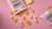 A flat lay of snack items against a pink background, featuring two open bags of protein chips with pieces scattered around. Several small cubes and a larger slice of cheese accompany the chips.