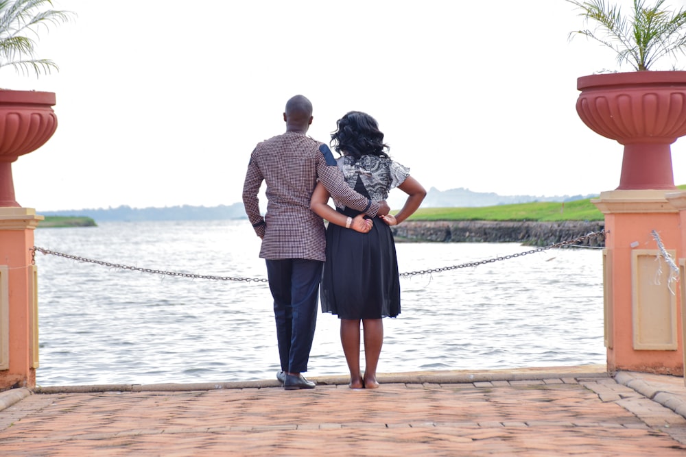 a man and a woman standing on a dock next to a body of water