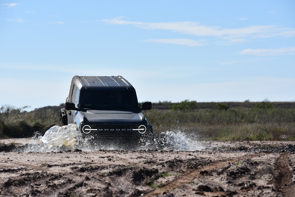 a black truck driving through a muddy field