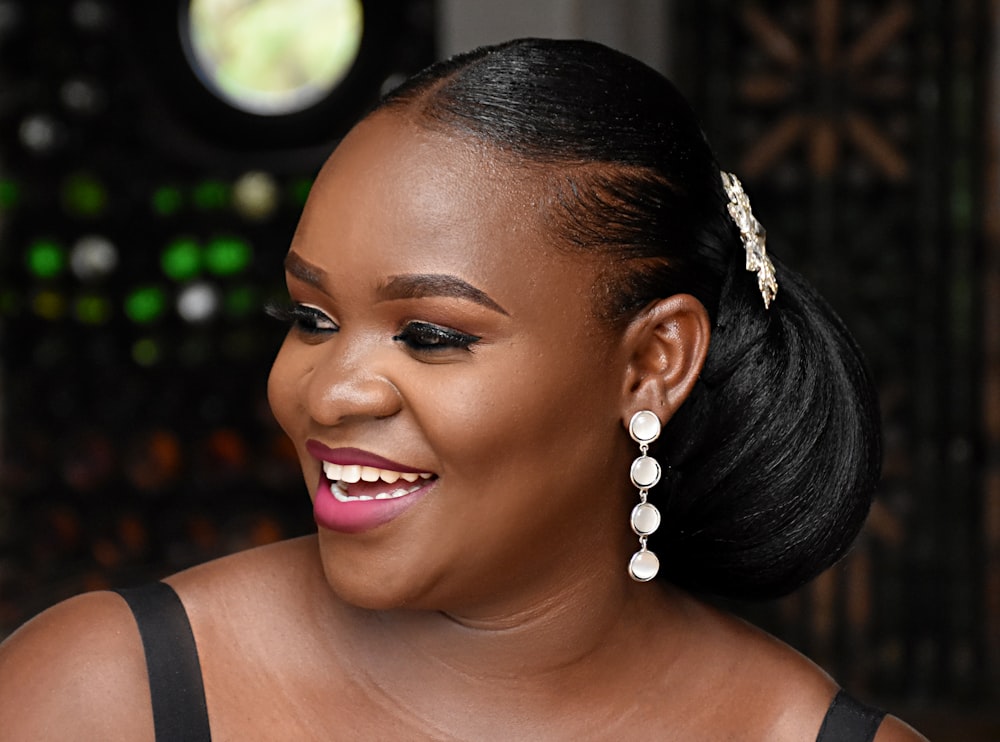 a woman in a black dress smiling and wearing a pair of earrings