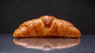 Close-up of a freshly baked golden croissant resting on a beige linen cloth with a dark pink background.