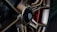 Close-up view of a stylish car wheel with a metallic alloy rim and a central black hub featuring detailed engravings. The wheel design is intricate, showcasing a blend of bronze tones against a red component in the background.