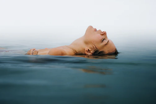 A person peacefully floating during a session, eyes closed, surrounded by tranquil water.
