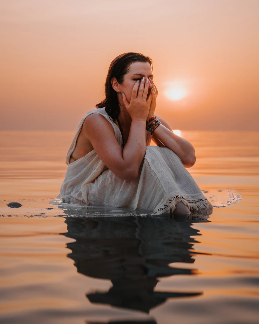 Mujer sentada en el agua con las manos en el rostro — introspección y proceso emocional