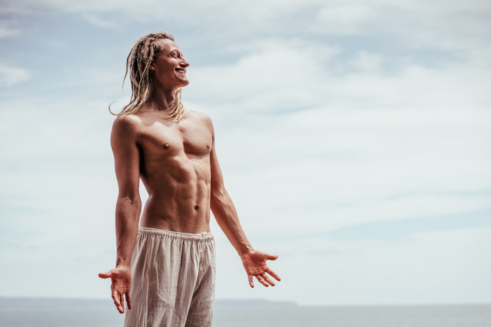 a shirtless man standing on a beach next to the ocean