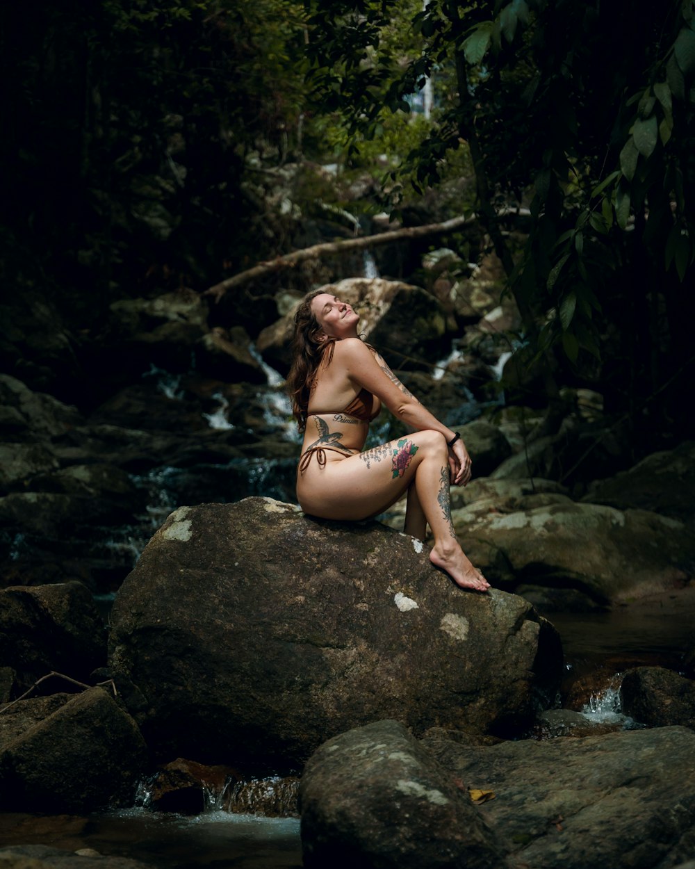 a woman in a bikini sitting on top of a rock