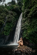 a woman sitting on a rock in front of a waterfall