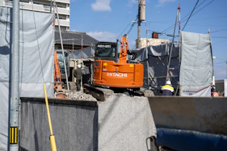 Technician installing a GPS tracker on a heavy-duty excavator at a busy construction site.