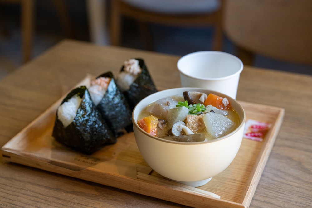 a wooden tray topped with a bowl of soup and a roll