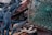 A collection of coiled and tangled ropes is intertwined with a green fishing net and rusted metal object. The ropes vary in color, with prominent shades of blue and white, while the net appears weathered and faded. The rusted metal adds a rugged and aged appearance to the scene.