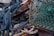 A collection of coiled and tangled ropes is intertwined with a green fishing net and rusted metal object. The ropes vary in color, with prominent shades of blue and white, while the net appears weathered and faded. The rusted metal adds a rugged and aged appearance to the scene.