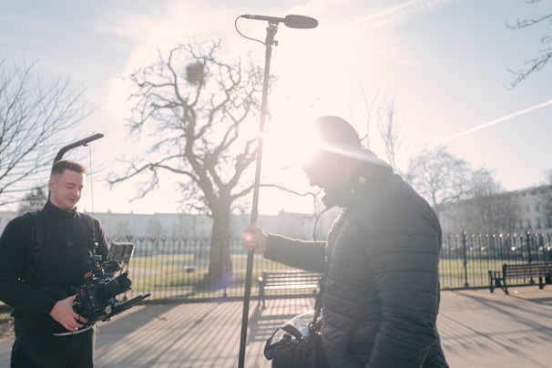 A cinematic frame showing a filmmaker directing a podcast recording in an open, sunlit field.