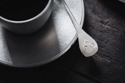 Close-up of a beautifully crafted coffee spoon resting on a rustic wooden table beside a steaming cup of coffee.