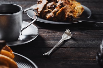 Close-up of a coffee cup next to a small homemade pastry on a rustic wooden table.