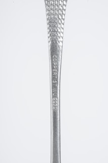A close-up view of a metallic object with a textured surface and engraved text reading 'COPPERIST.WU S925'. The handle tapers from narrow to wide, showcasing a shiny silver finish against a plain background.
