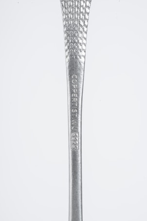 A close-up view of a metallic object with a textured surface and engraved text reading 'COPPERIST.WU S925'. The handle tapers from narrow to wide, showcasing a shiny silver finish against a plain background.