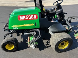 A green John Deere vehicle with a red MK5G68 label and a 3235C model designation parked on a paved surface. It features large black and yellow wheels and visible mechanical components, including hoses and metallic parts.